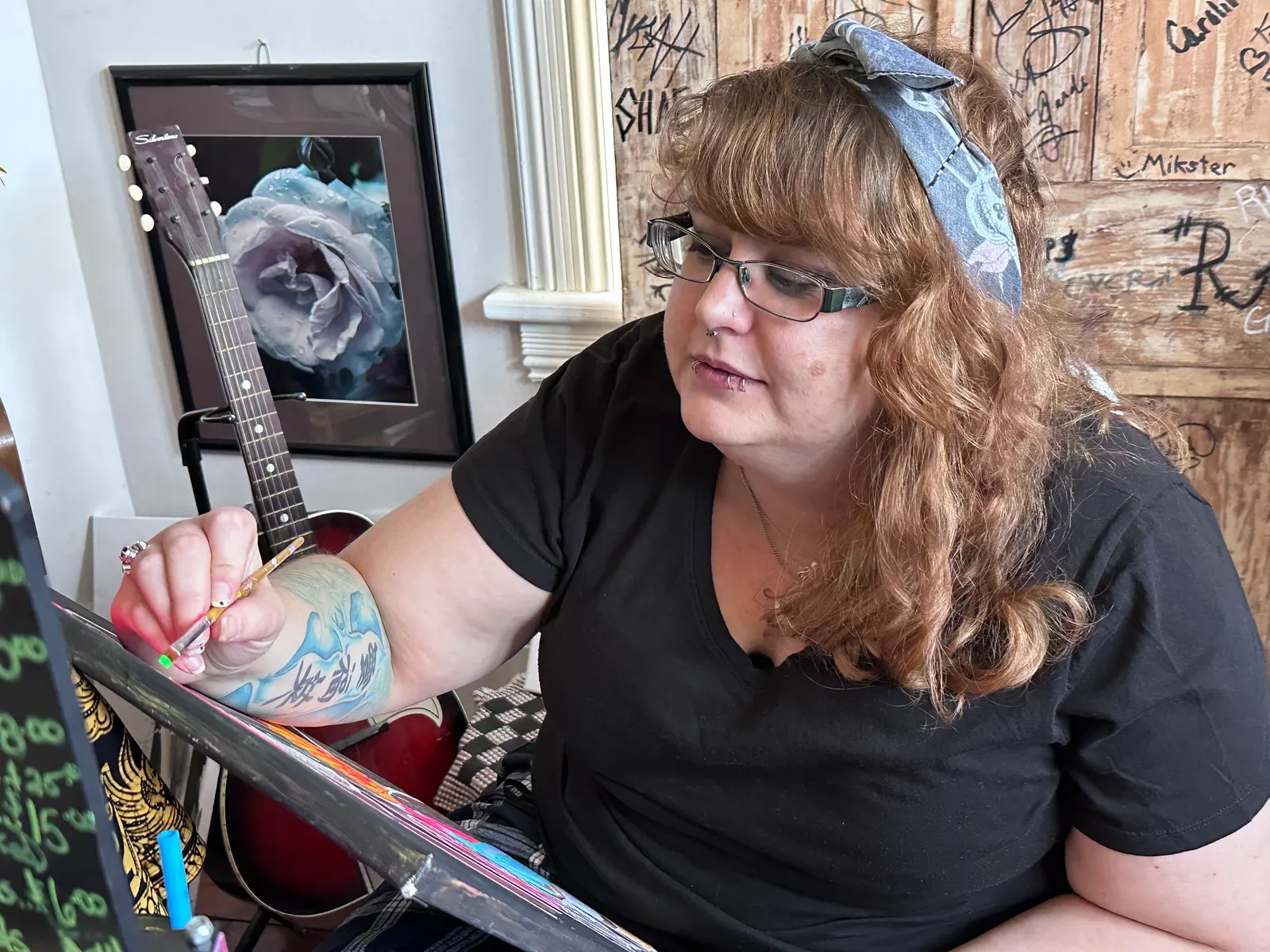 A woman paints at an easel in the front room, with a guitar and artwork on the wall behind her