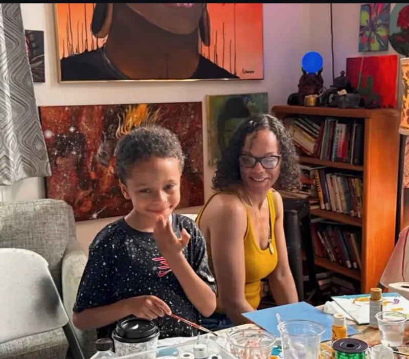 A smiling boy and his mom paint together beneath a wall of portraits