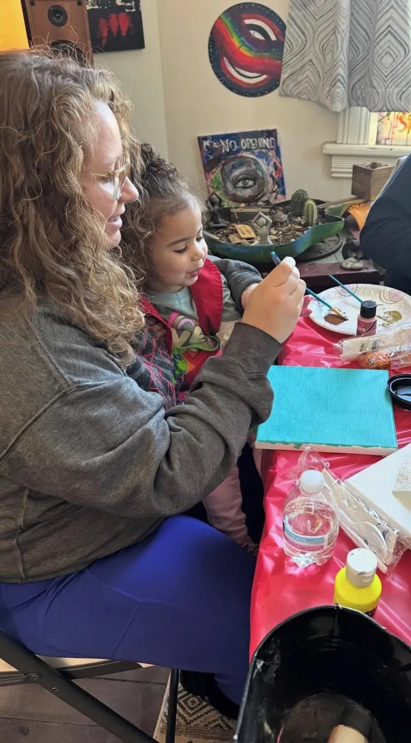 A mom holds her toddler on her lap while they paint together at a Clarity House art table