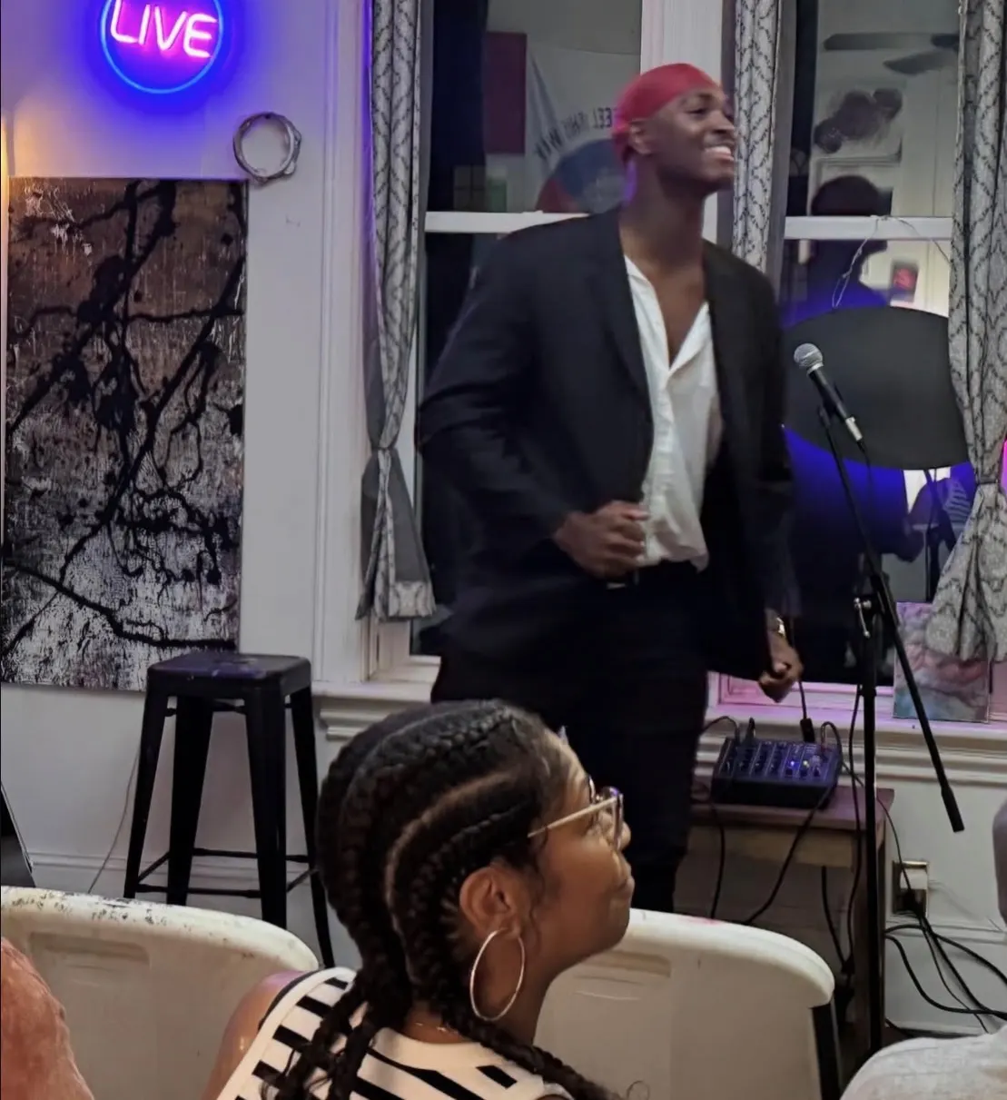 A singer performs at a mic under a neon LIVE sign
