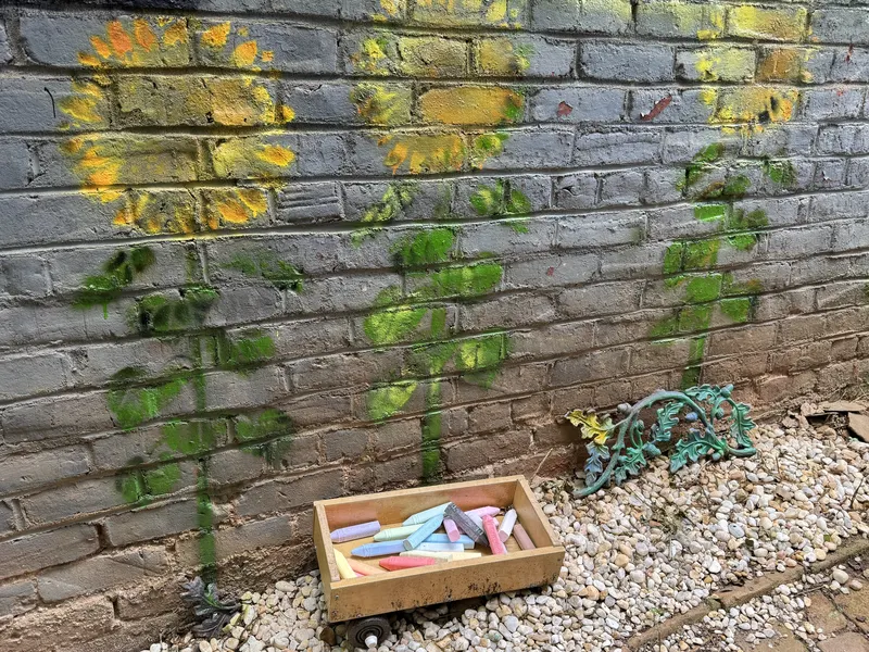 Sunflowers painted on the brick wall of the Rachel Burns Zen Garden with a box of chalk below